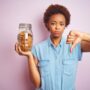 African american woman holding jar of chocolate chips cookies over pink isolated background with angry face, negative sign showing dislike with thumbs down, rejection concept