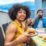 Woman holding burger while enjoying rooftop barbecue with friends